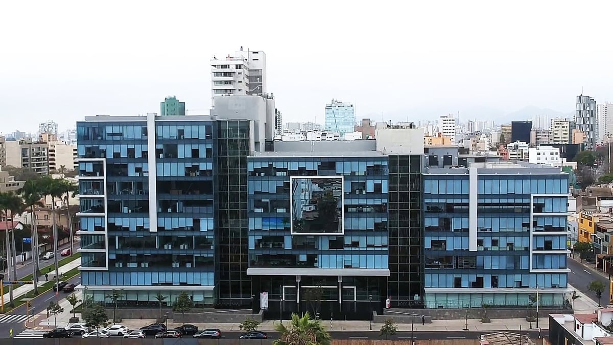 Modern multi-story blue glass residential building with urban skyline and parked cars in front