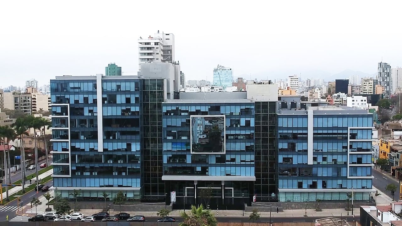 Modern multi-story blue glass residential building with urban skyline and parked cars in front