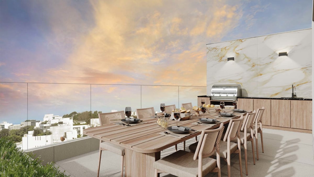 Modern rooftop terrace with wooden dining table, chairs, and kitchen area overlooking cityscape at sunset