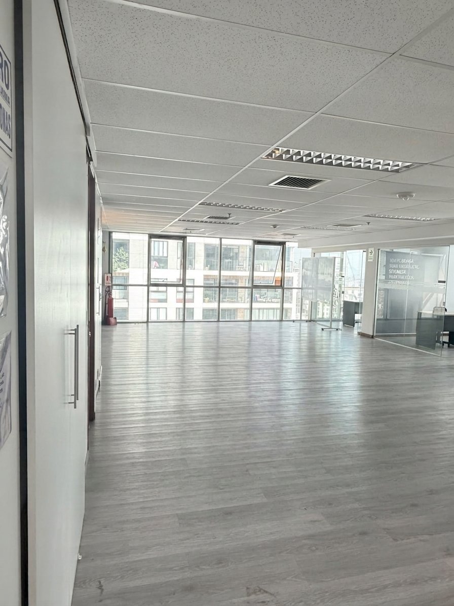 Espacio de oficina o retail vacío con piso de gris claro, cielo raso blanco y ventanales de piso a techo a lo largo de la pared