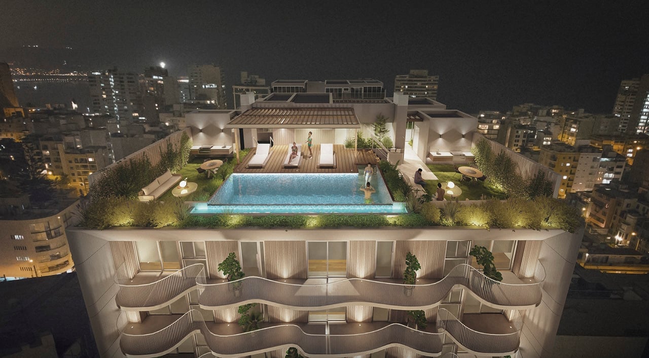 Aerial nighttime view of a luxury rooftop with illuminated swimming pool, lounge areas, and landscaping overlooking a city skyline