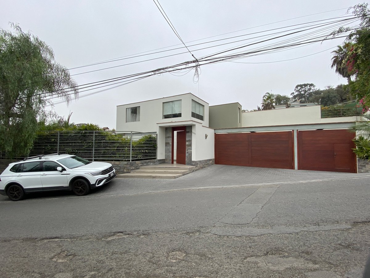 Modern two-story white house with red metal garage doors and white car parked in front on a residential street