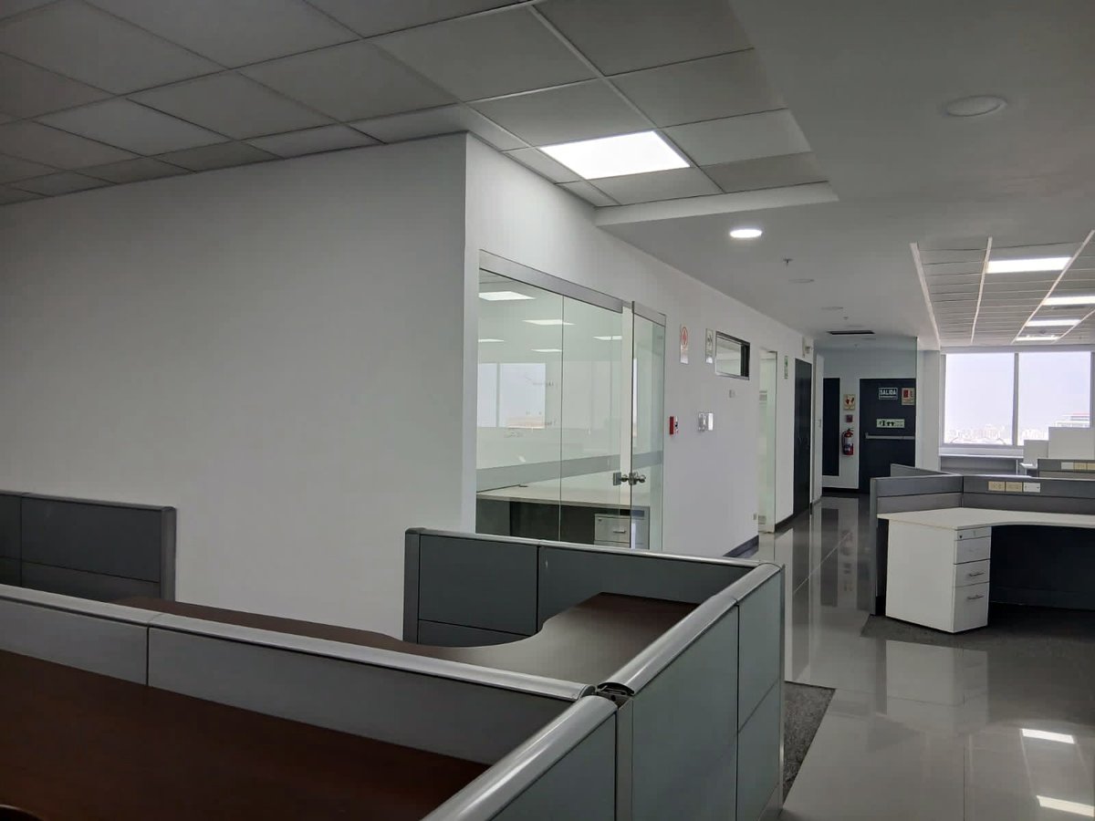 Modern office reception area with glass partition walls, desk counter, and open workspace visible in background