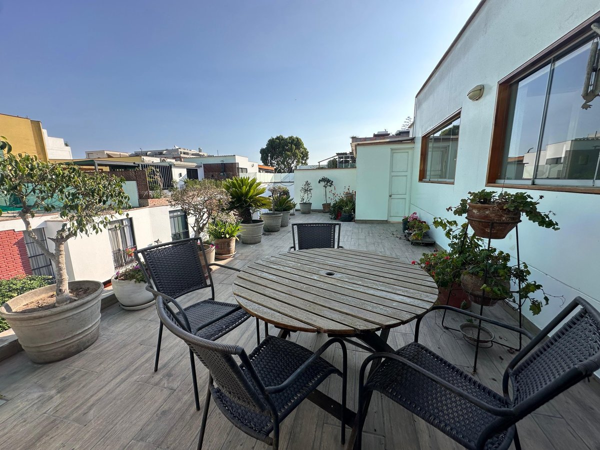 Rooftop terrace with black patio furniture, round table, and potted plants overlooking urban residential buildings