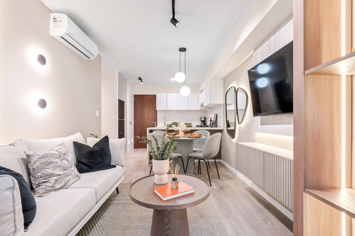 Modern studio apartment with sleeping area on left, dining table center, and kitchen with mounted TV on right wall