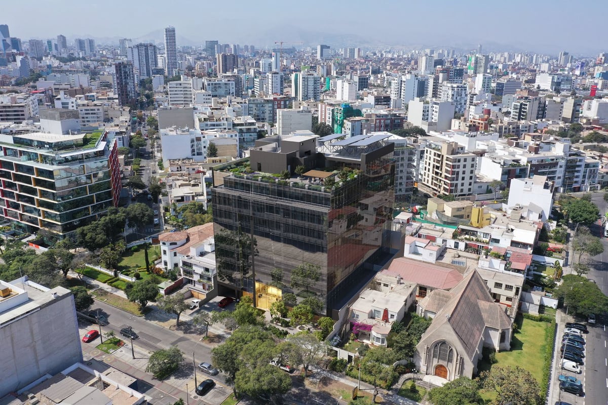 Aerial view of a dense urban cityscape with mixed modern and older buildings, green spaces, and skyscrapers in the background