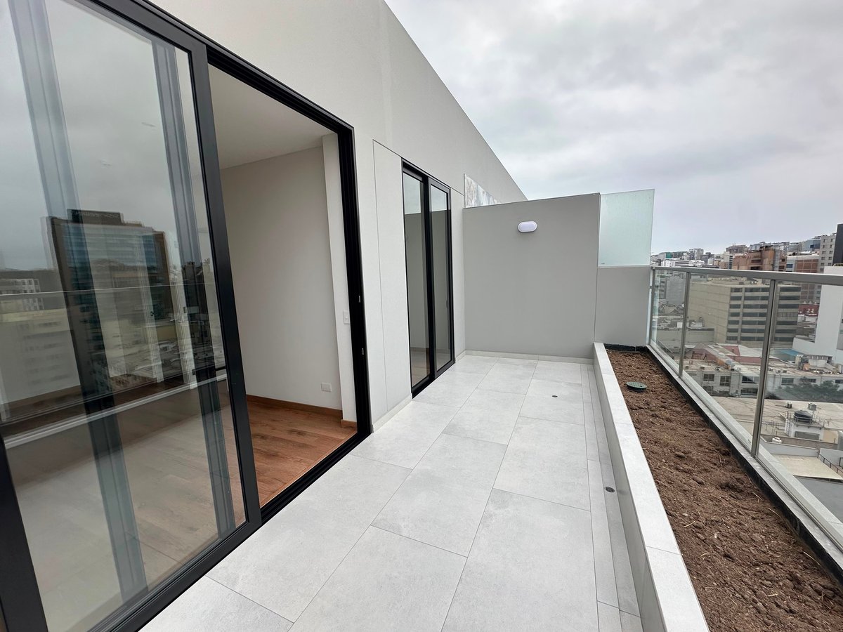 Modern high-rise apartment balcony with sliding glass doors, white tile flooring, and city skyline view