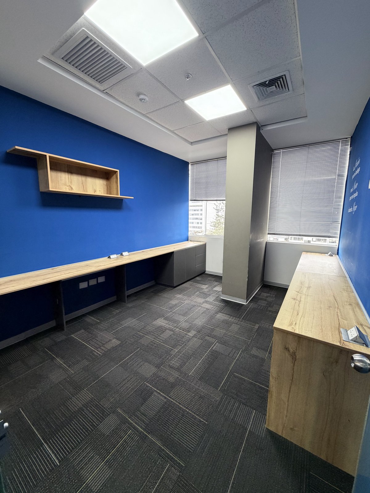 Modern office interior with bright blue walls, wood desks, ceiling lights, and gray tile flooring