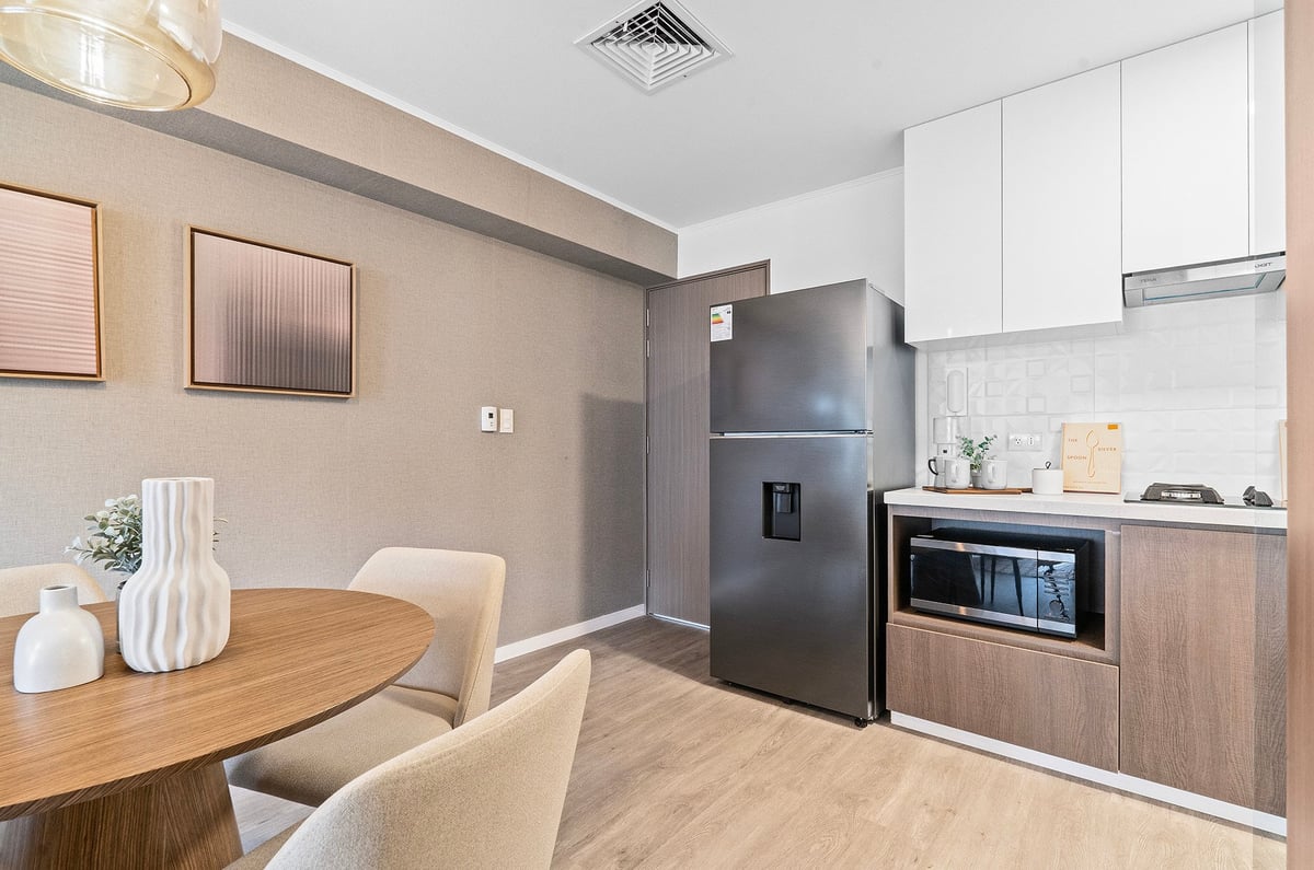 Modern kitchen and dining area with wood table, beige chairs, stainless steel appliances, and white cabinetry