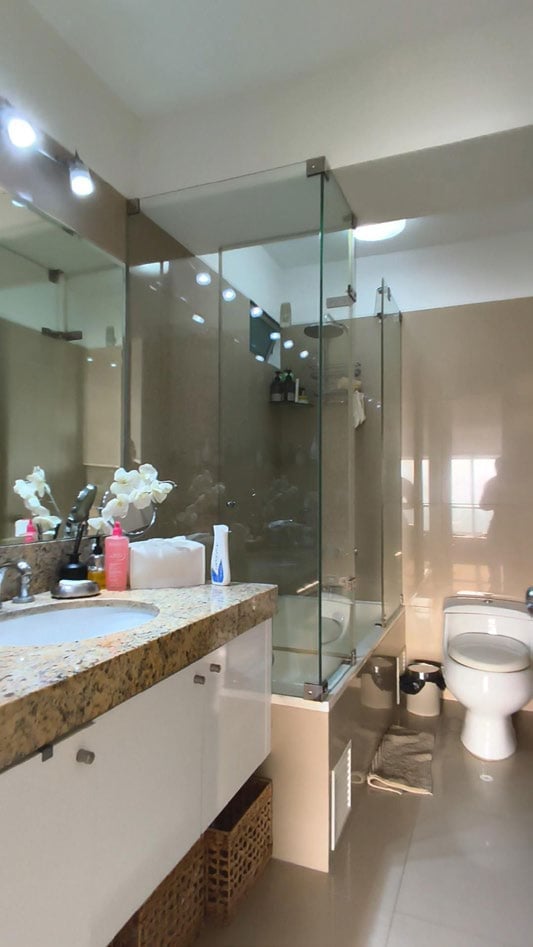 Modern bathroom with granite sink countertop, large mirror, glass shower enclosure, and white toilet