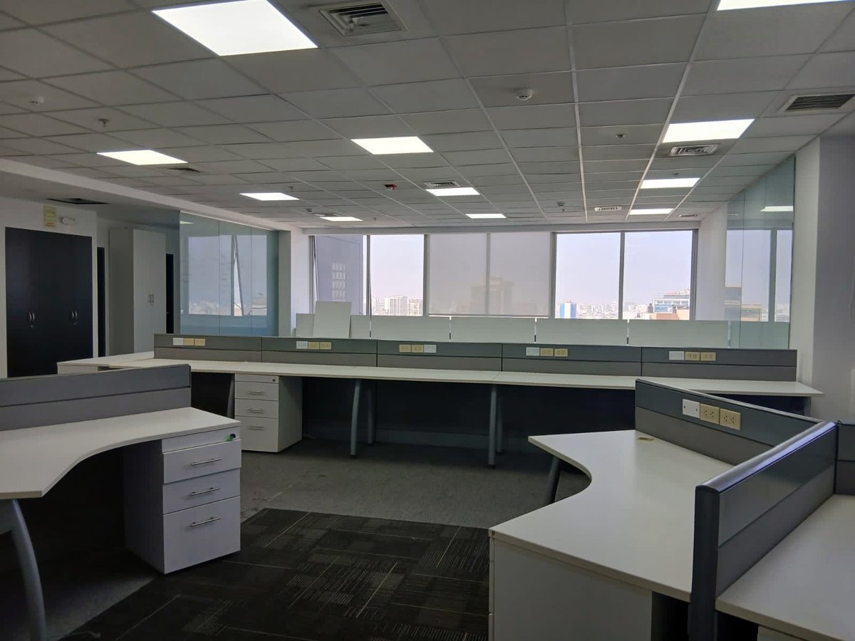 Empty modern office space with desks, filing cabinets, and glass-walled partitions under fluorescent lighting