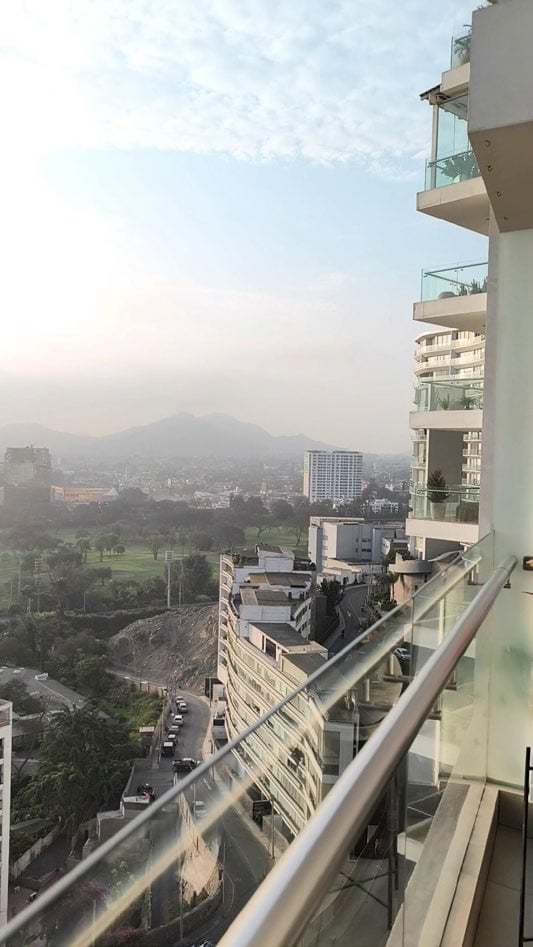 View from a high-rise apartment balcony overlooking a hazy cityscape with a mountain in the distance and green areas below