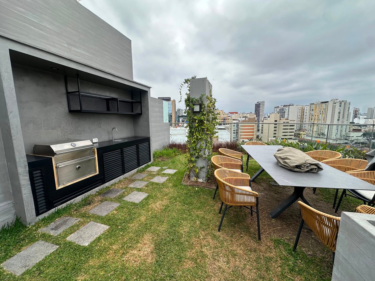 Modern rooftop terrace with outdoor kitchen, dining table, chairs, grass, and city skyline view