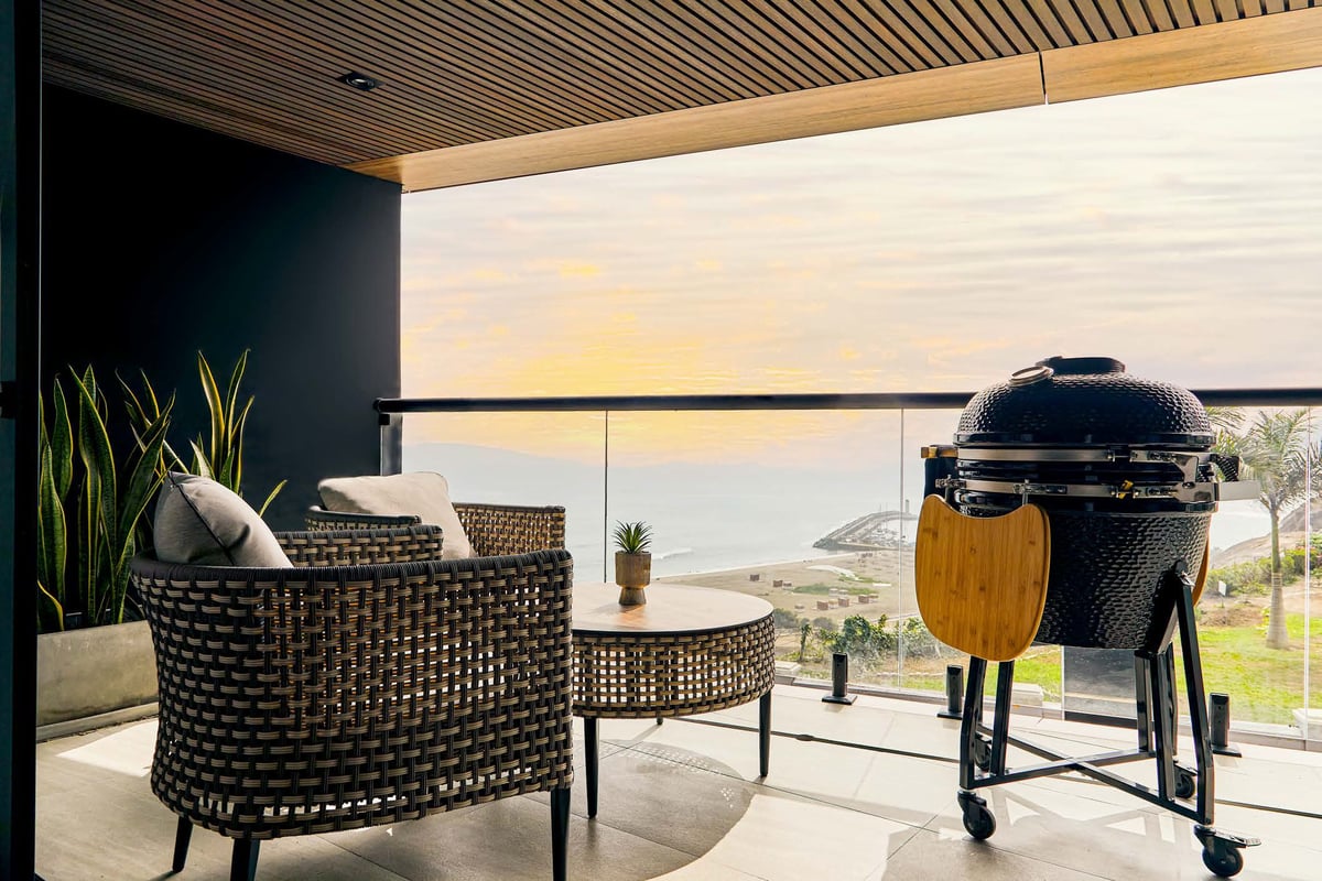 Modern patio with woven chair, side table, and black dome grill overlooking scenic landscape at sunset