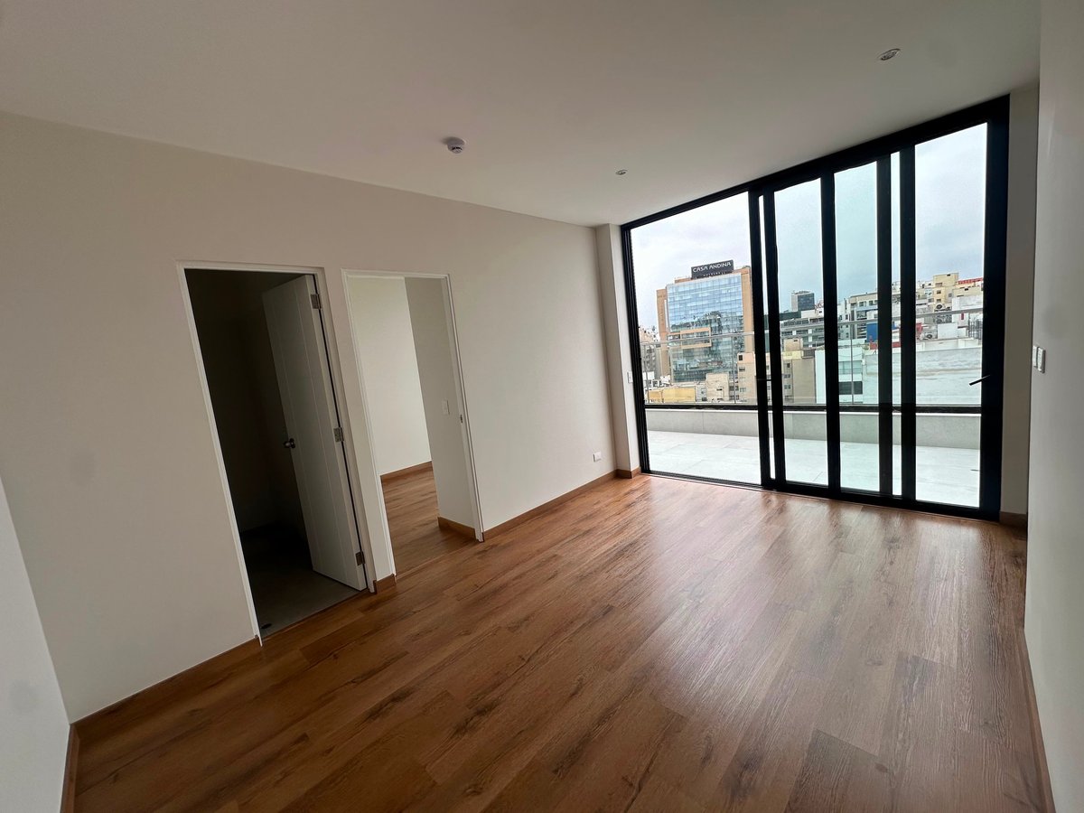 Empty modern apartment interior with wooden floors, white walls, and large floor-to-ceiling windows overlooking a city skyline