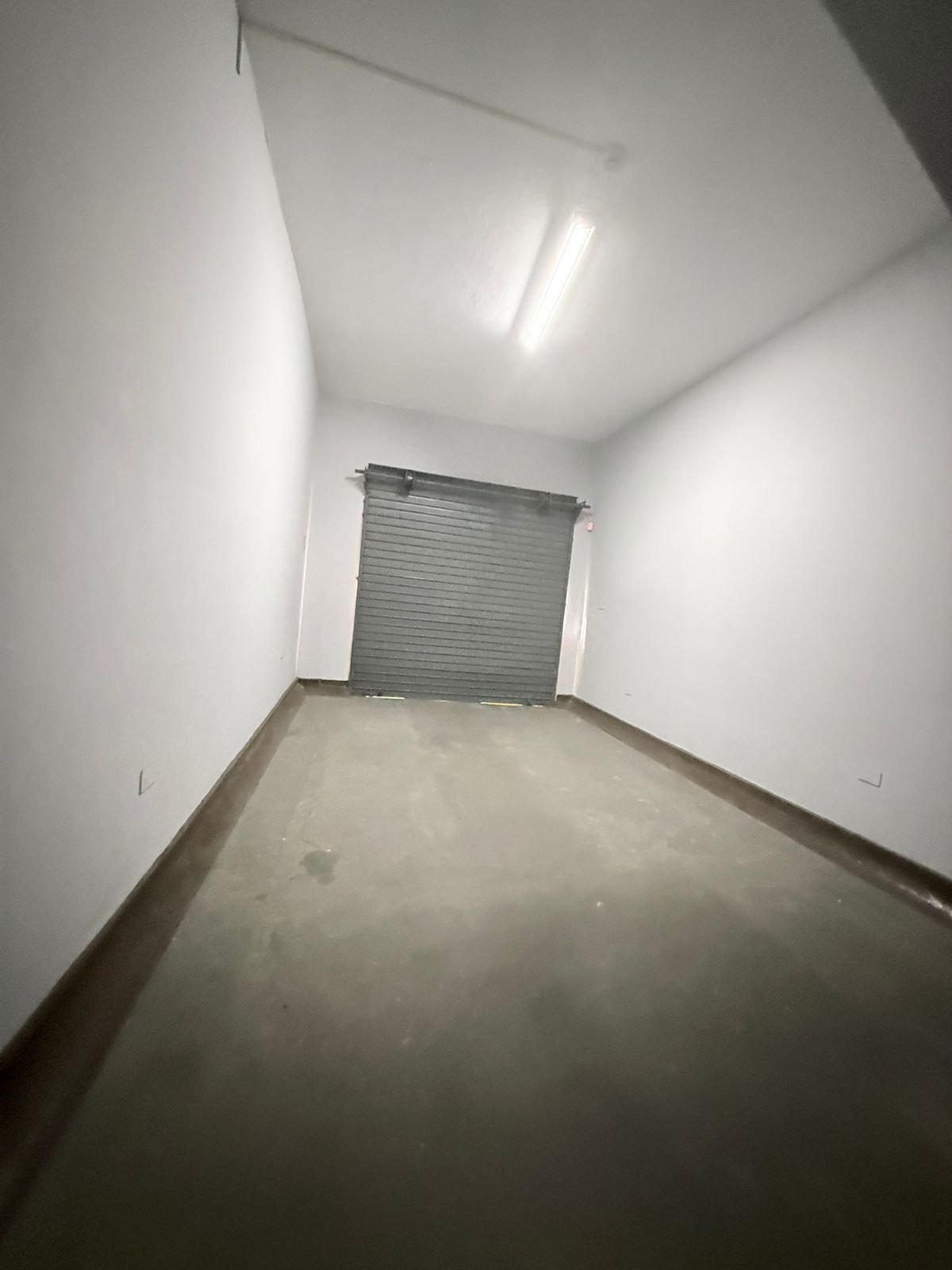 Empty garage interior with white walls, fluorescent ceiling light, and metal roll-up door