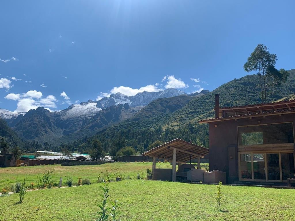 Modern building with red roof on green valley floor, surrounded by forested mountains under blue sky with clouds