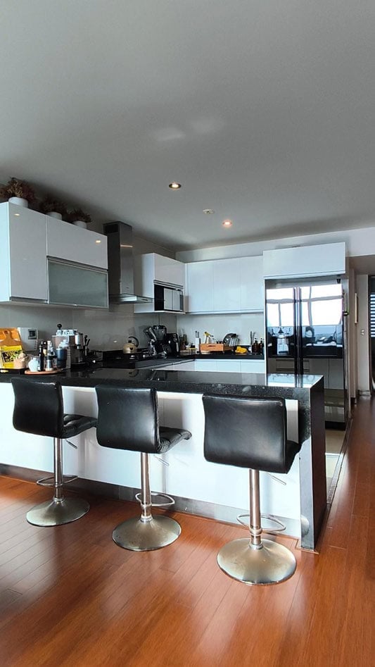 Modern kitchen with white cabinets, black countertops, island with black bar stools, and wooden flooring
