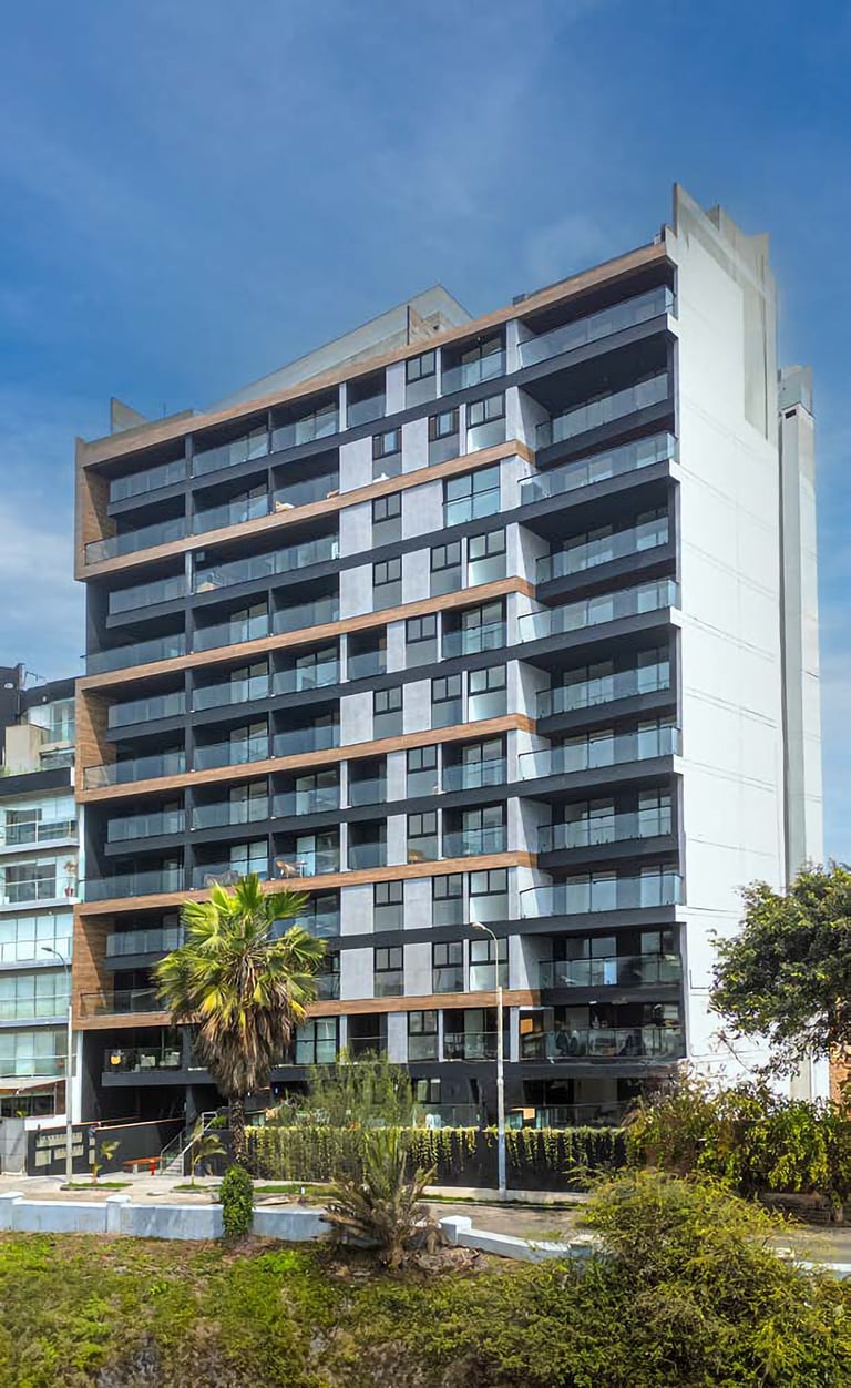 Modern residential apartment building with white and dark facade, glass balconies, and wooden trim accents against blue sky