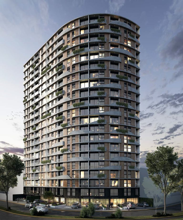 Modern cylindrical residential high-rise apartment building with lit windows at dusk, surrounded by street-level landscaping and parked vehicles