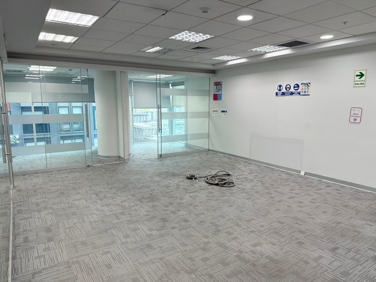 Empty office or retail space with glass doors, frosted glass partitions, drop ceiling lights, and gray tile flooring