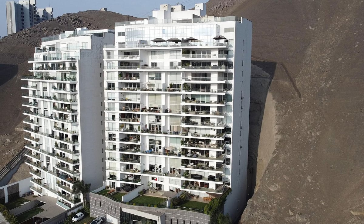 Modern white residential high-rise apartment building with balconies overlooking a hillside with sparse vegetation