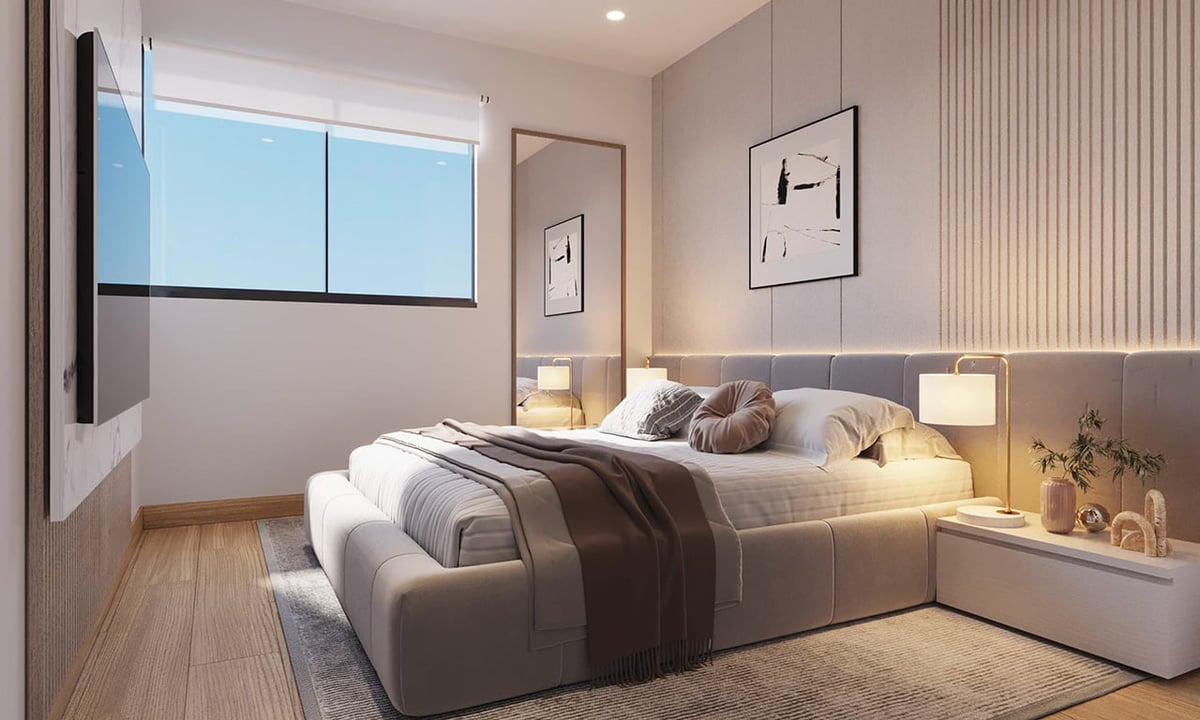 Modern bedroom with gray upholstered bed, wooden floor, wall-mounted TV, nightstands with lamps, and large windows overlooking city skyline