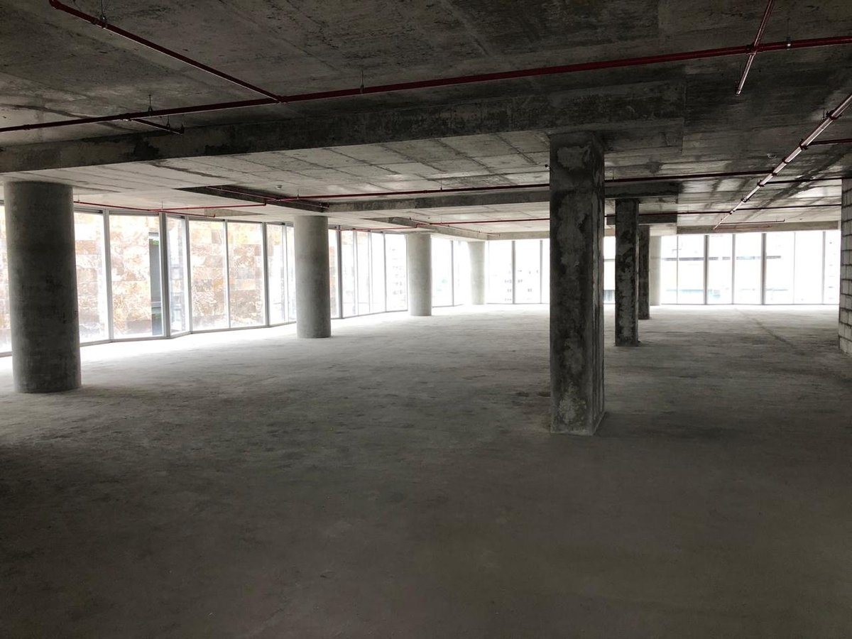 Empty concrete floor of an unfinished building interior with support columns, exposed ceiling, and large windows