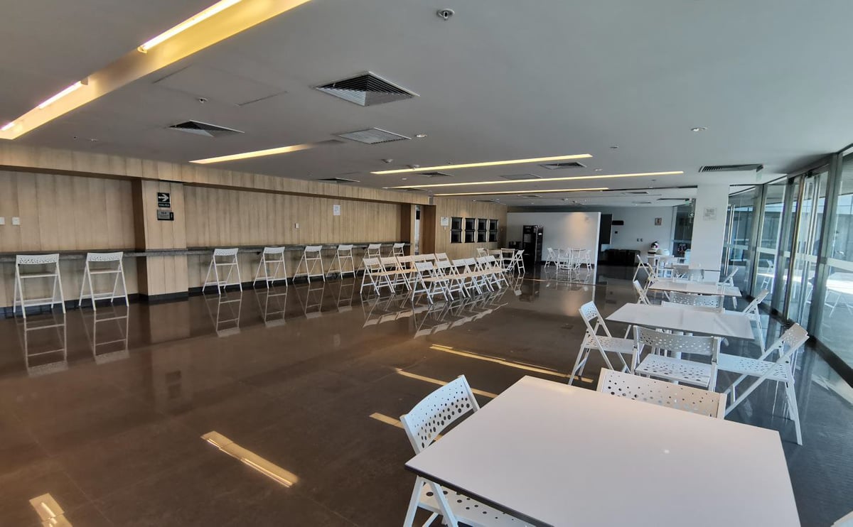 Empty event space with white tables and chairs, wood flooring, and large windows with modern ceiling lights