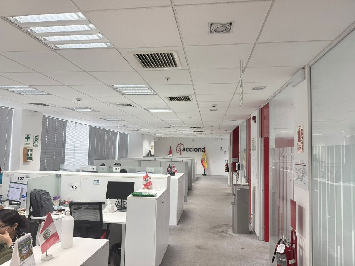 Modern office hallway with white cubicles, fluorescent ceiling lights, and red accents on doors and signage