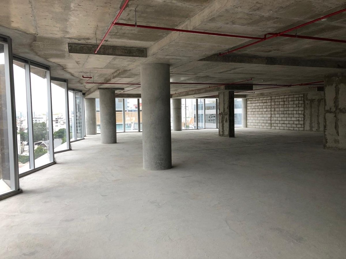 Empty concrete commercial space with exposed ceiling, support columns, and large windows overlooking street