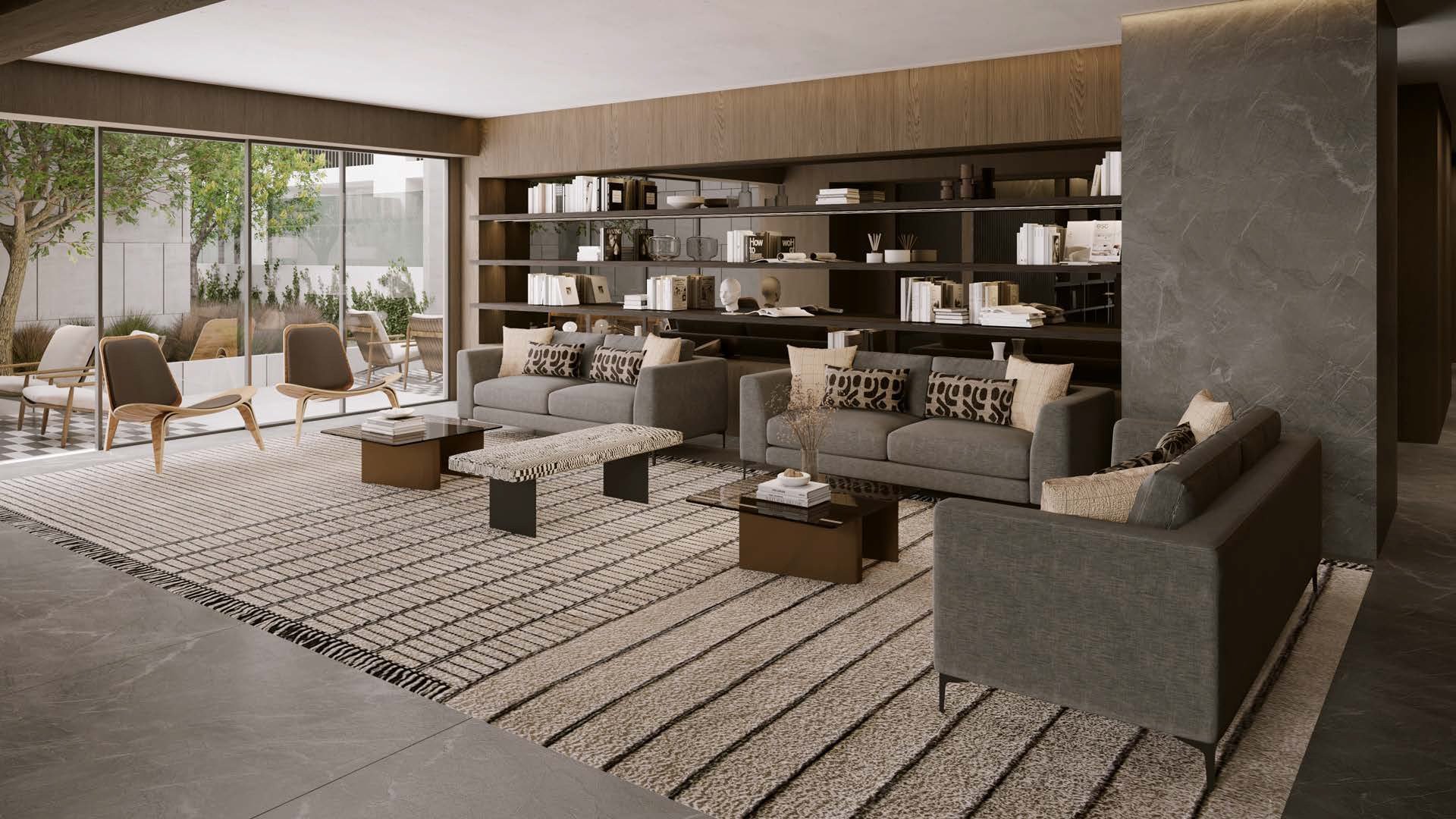 Modern minimalist living room with gray upholstered furniture, built-in shelving, geometric area rugs, and floor-to-ceiling windows overlooking nature