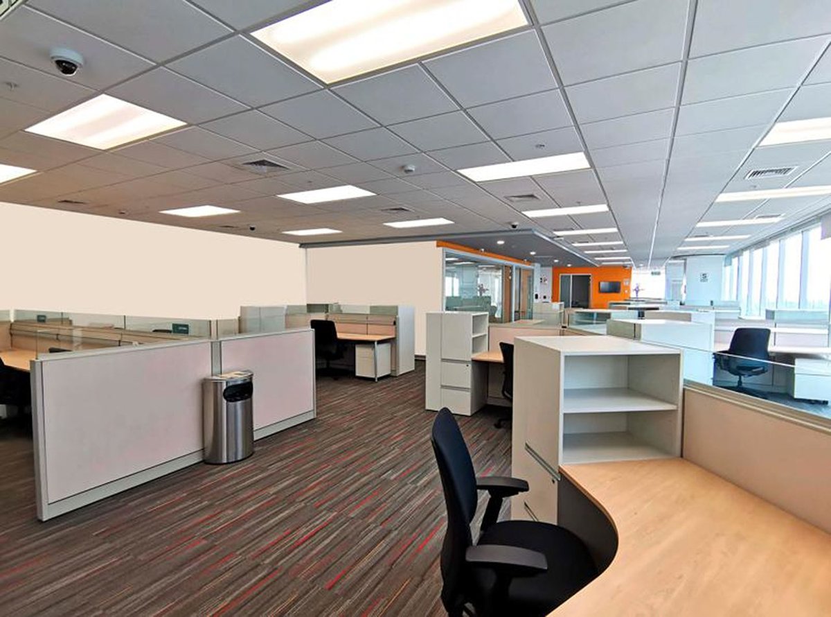 Modern office space with cubicles, white desks, black chairs, drop ceiling lighting, and floor-to-ceiling windows