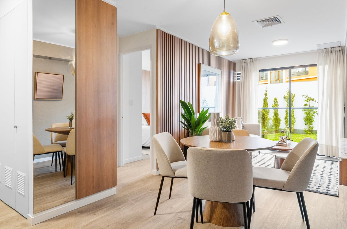 Modern dining room with wooden table, beige chairs, pendant lighting, and wood slat partition with potted plants and windows