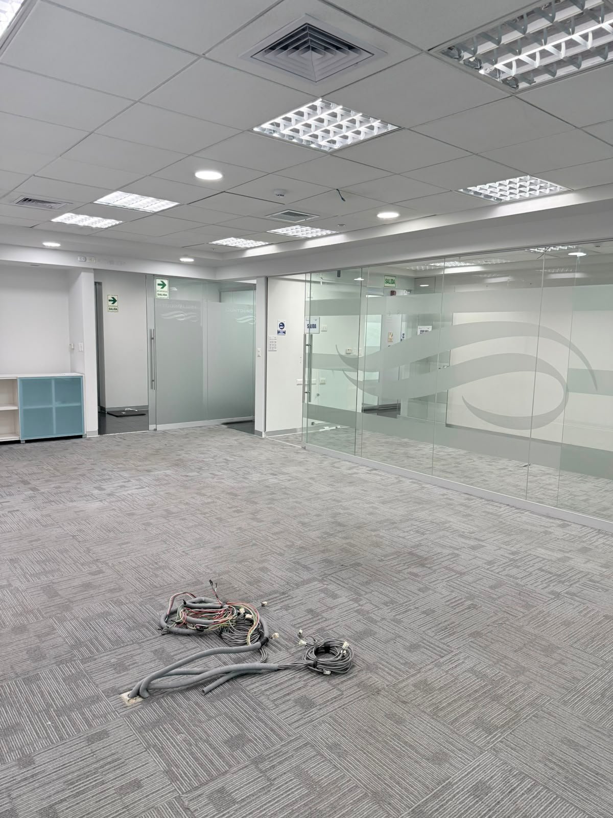 Empty modern office interior with glass partitions, fluorescent ceiling lights, and cables on gray tile floor