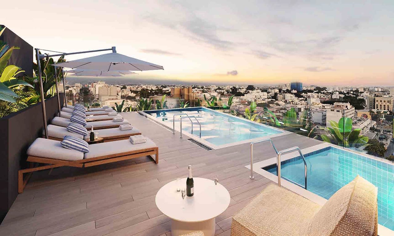 Rooftop pool deck with lounge chairs, umbrella, and city skyline view at sunset