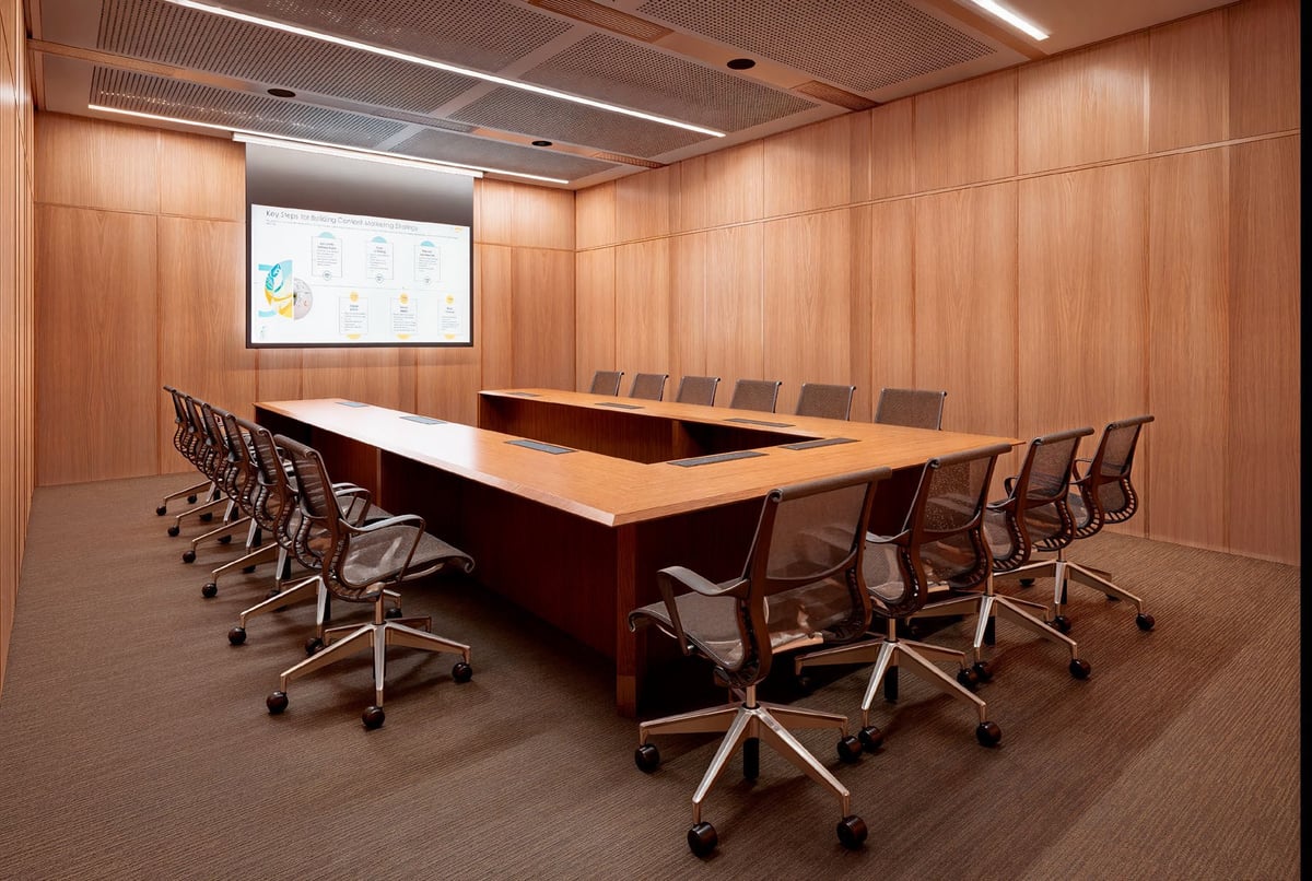 Modern conference room with wood paneling, large table, ergonomic chairs, and presentation screen on wall.