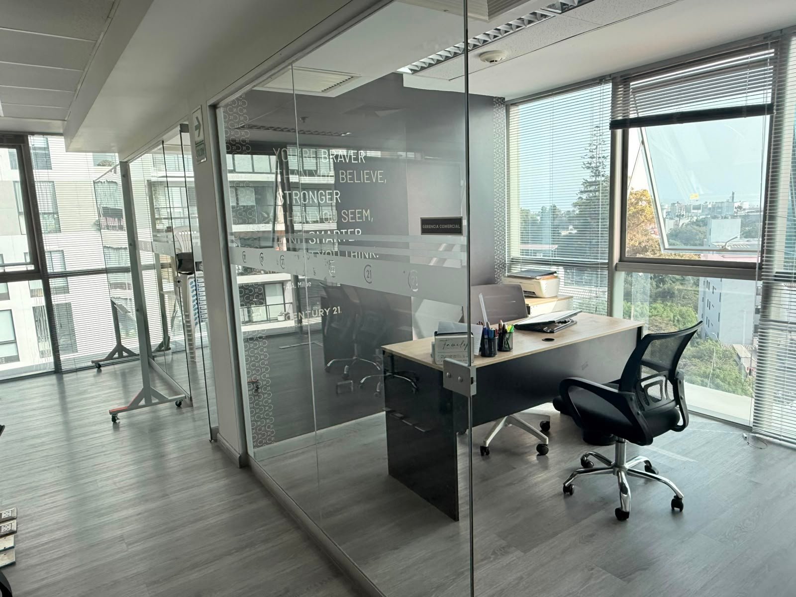 Oficina moderna con cubículo de pared de vidrio, escritorio y vista a la ciudad desde ventana en torre