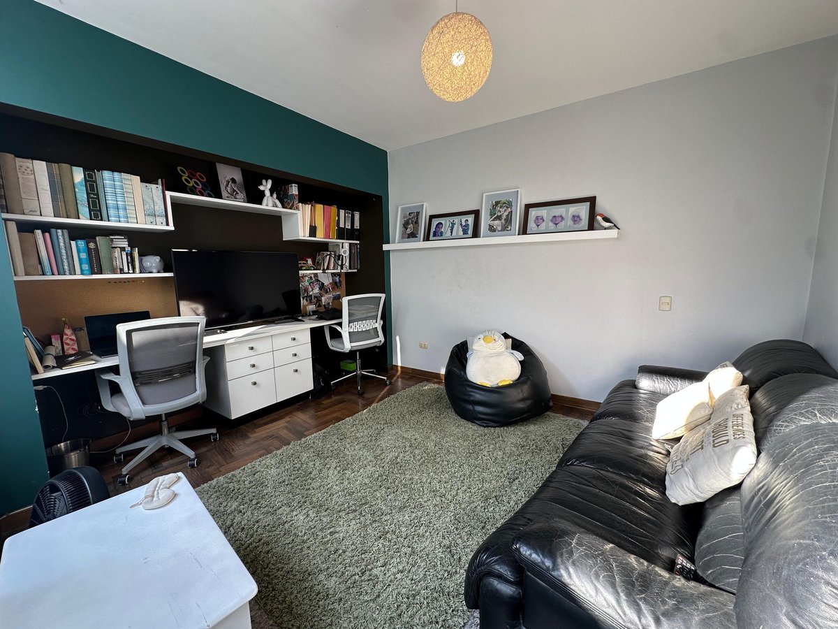 Modern bedroom with teal accent wall, built-in desk with shelves, bed with pillows, bean bag chair, and woven ceiling lamp.