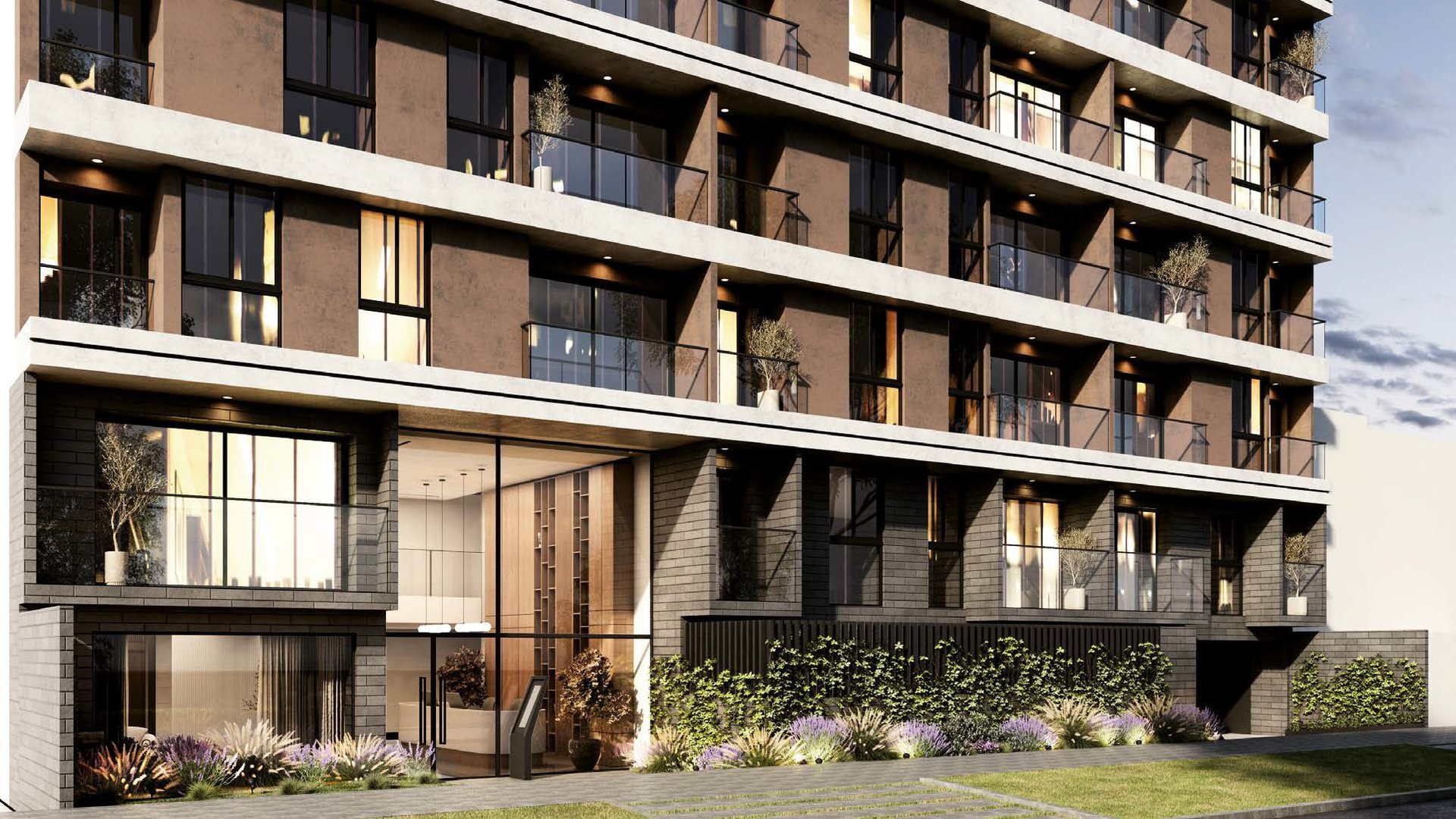 Modern multi-story residential building with brown and glass facade, balconies, and ground-level landscaping at dusk