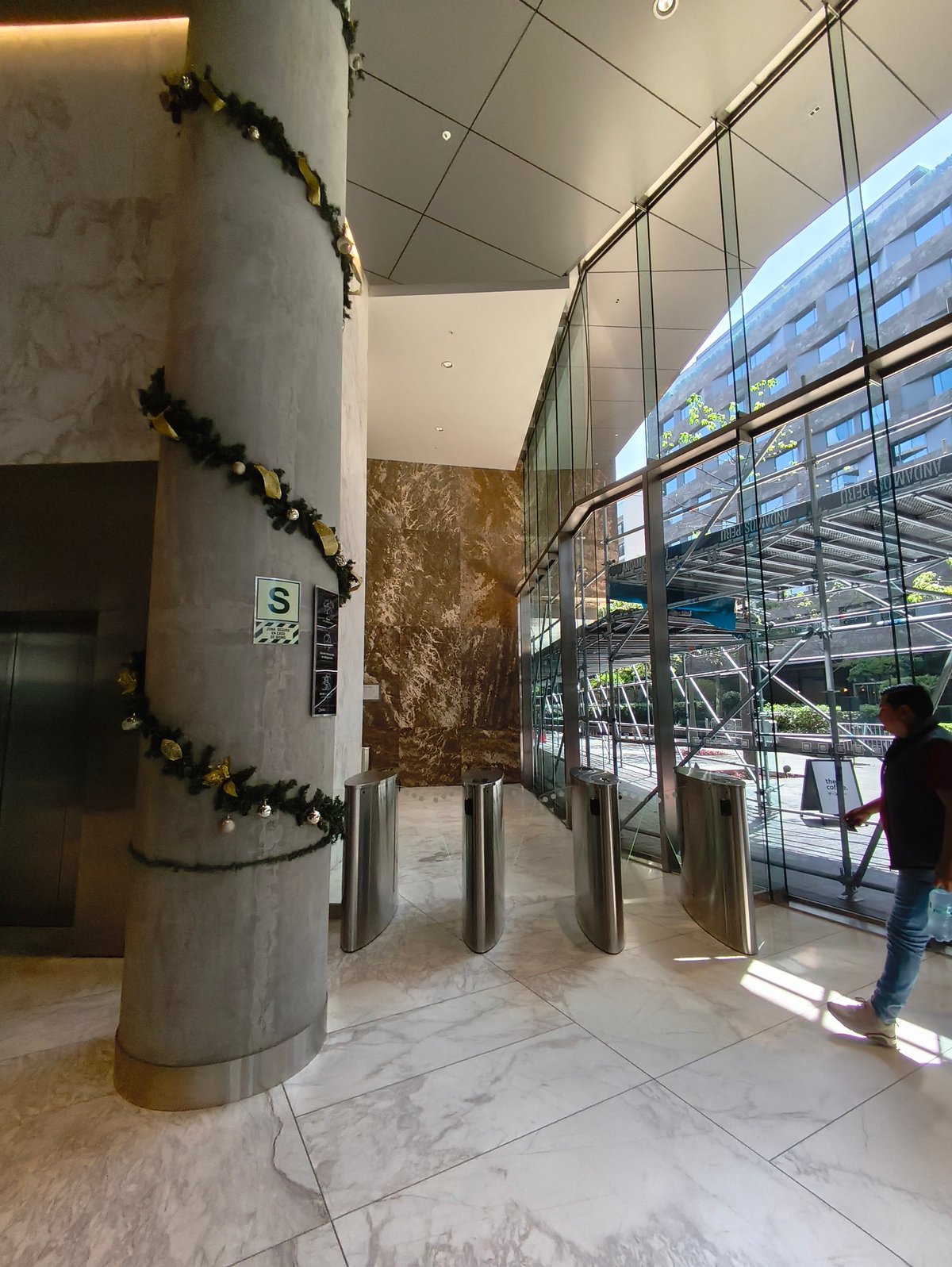 Modern building lobby with circular concrete column decorated with garland, glass walls, and metal railings