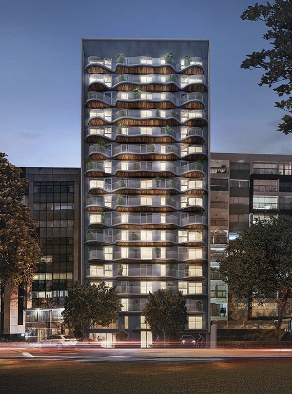 Modern residential tower with curved balconies, illuminated windows, flanked by historic buildings at dusk with light trails