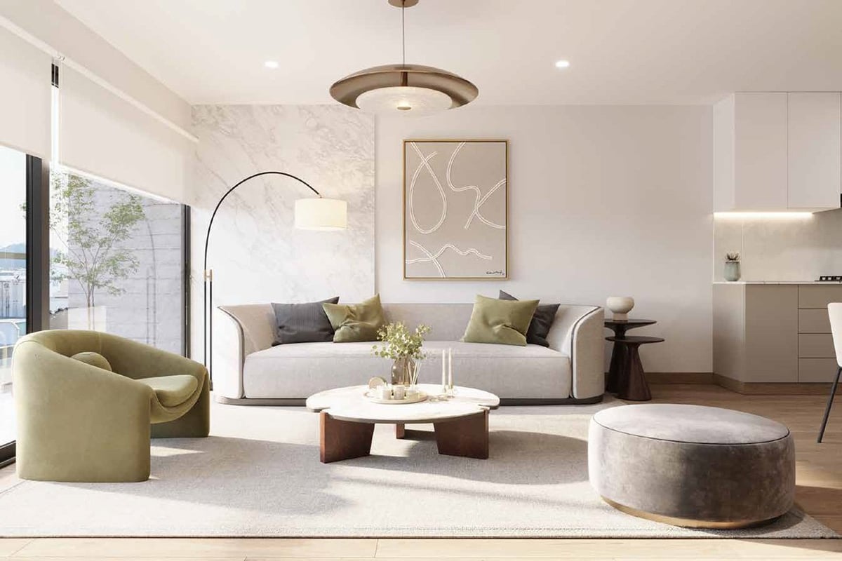 Modern living room with beige sofa, gold armchair, round coffee table, and coordinating ottoman in neutral tones with large windows and pendant lighting