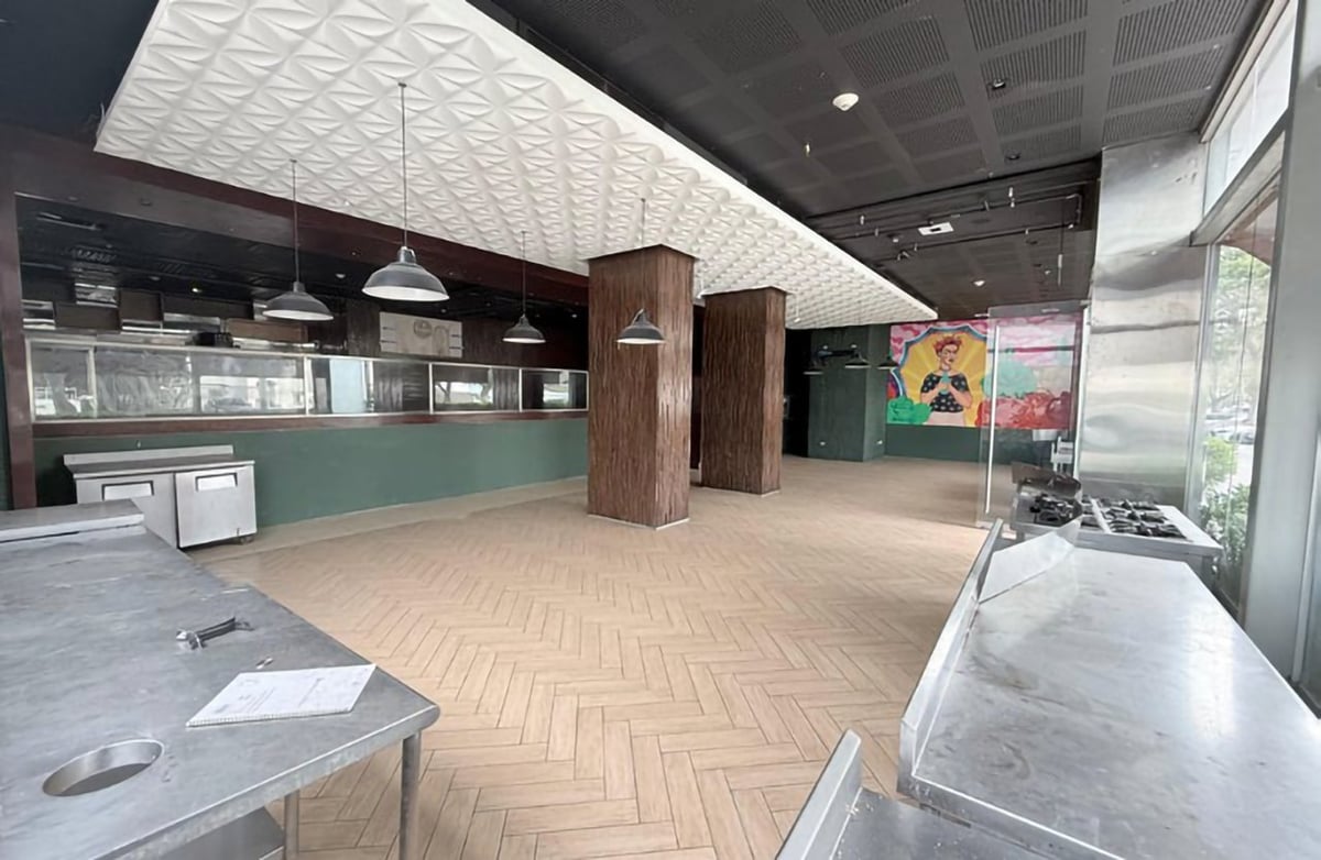 Empty retail space with herringbone flooring, wooden columns, modern lighting, and service counter visible in background