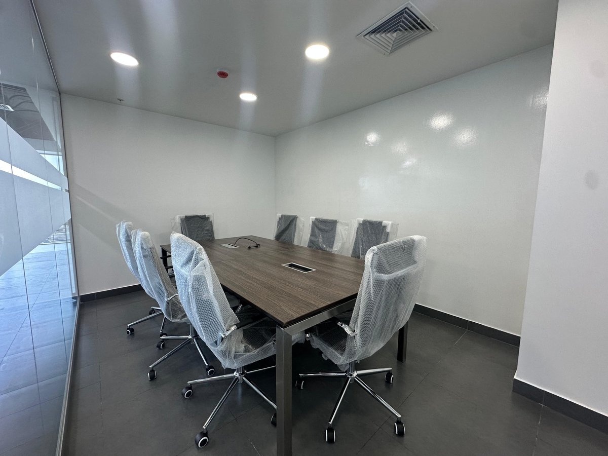 Modern conference room with rectangular wood table surrounded by white wrapped office chairs and whiteboard on side wall