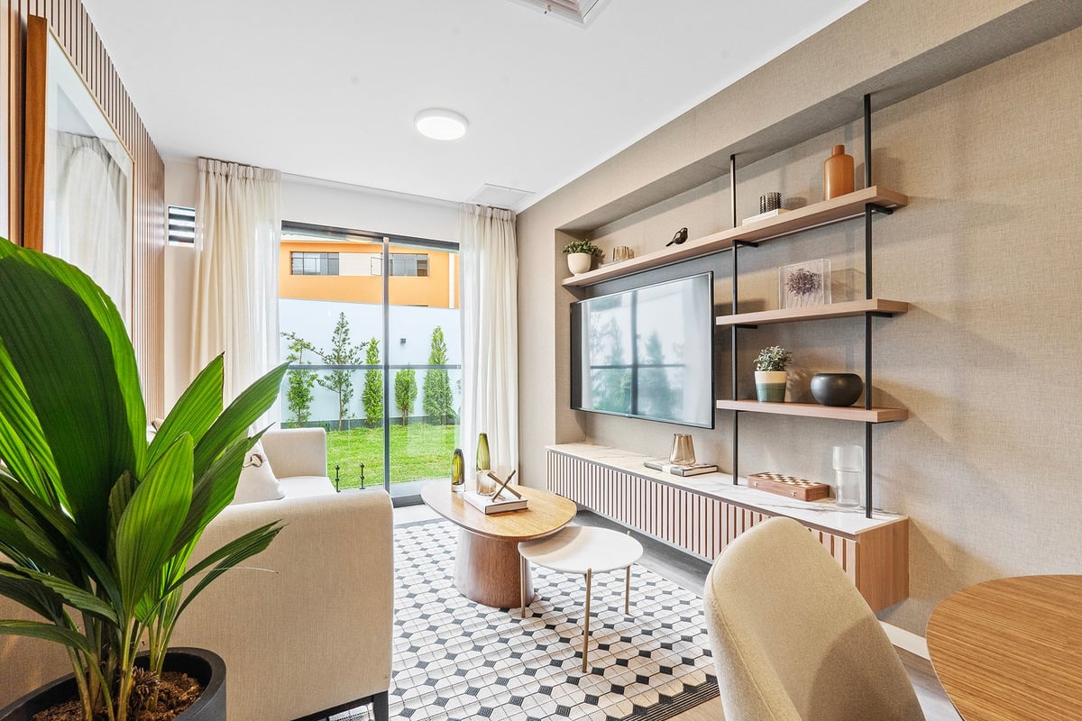 Modern living room with cream furniture, floating shelves with decor, large windows overlooking greenery, geometric floor tiles, and potted plant
