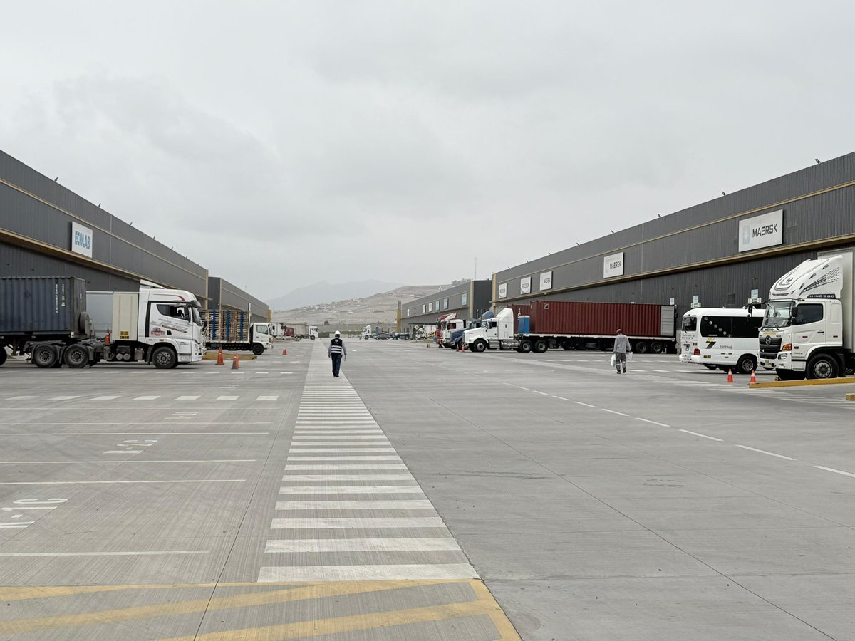 Industrial warehouse complex with multiple trucks parked along loading docks under cloudy sky