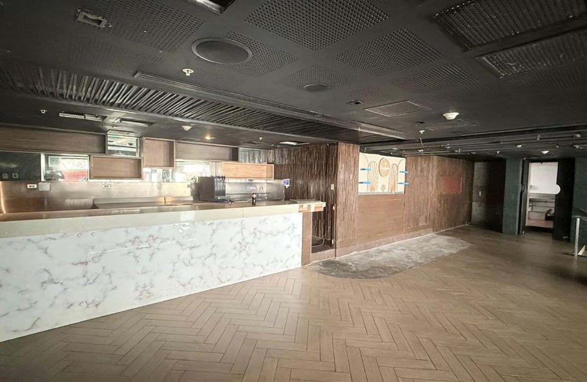 Empty restaurant or retail space with marble front counter, herringbone flooring, and industrial ceiling with recessed lighting.