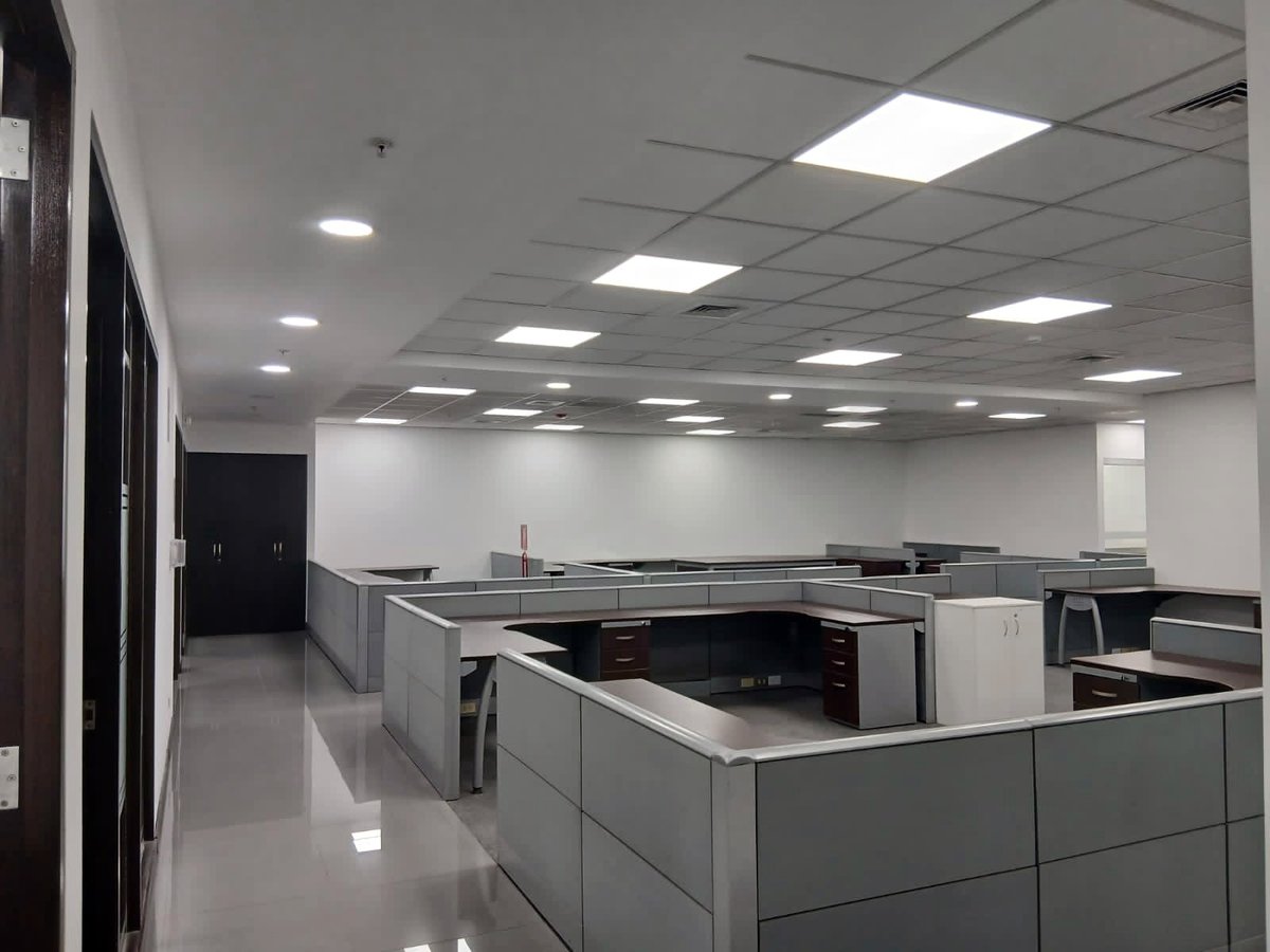 Empty modern office space with gray cubicles, fluorescent ceiling lights, and polished white flooring