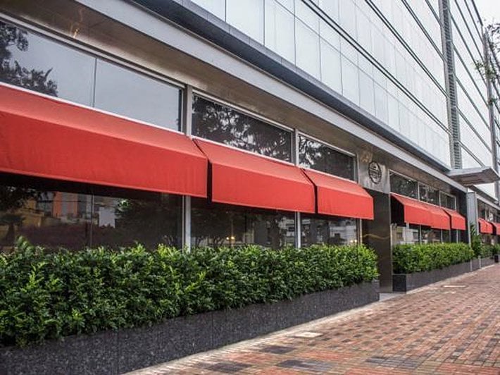 Storefront with red awning and large windows, landscaping bushes below, brick walkway in foreground